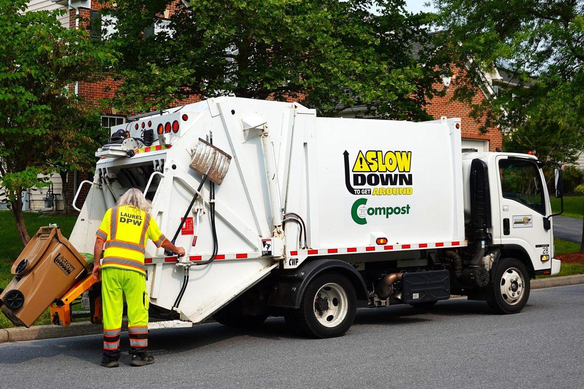 Man in bright yellow loads compost into large white truck marked Laurel Compost