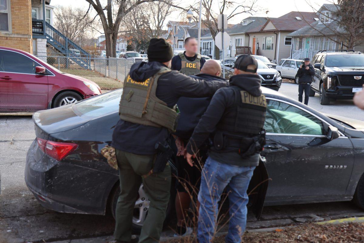 3 men in street clothes with police vests stand around a car while detaining a 4th man in civilian clothes in a residential neighborhood.
