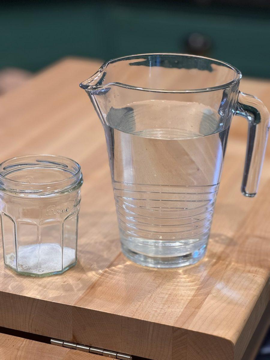 A glass pitcher of water sits next to a drinking glass with a small amount of salt in it.